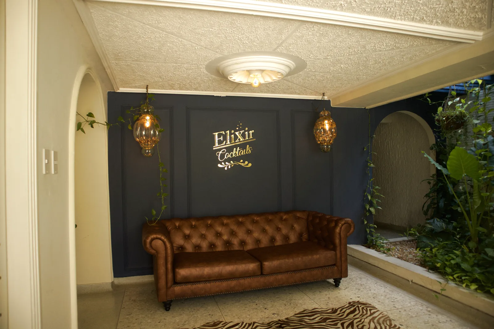 Lounge con sofá chesterfield y pared azul con letrero Elixir Cocktail